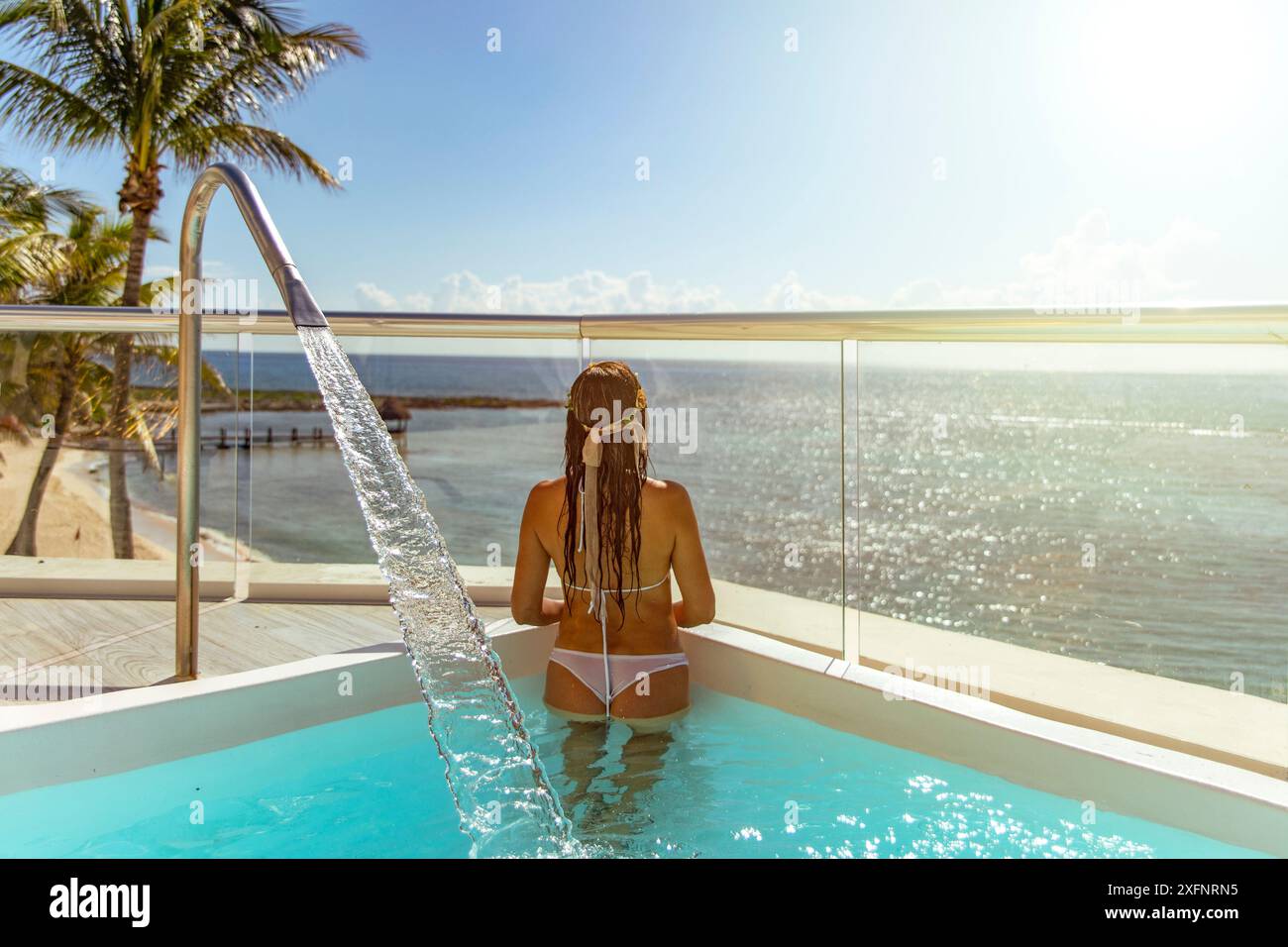 Giovane donna turistica che si gode il meraviglioso orizzonte del Mar dei Caraibi, sotto un sole splendente che riflette le acque cristalline blu turchese. Foto Stock