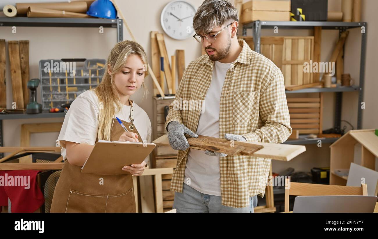 Uomo e donna in officina che ispezionano il legno con gli attrezzi intorno, trasportando il lavoro di squadra e le abilità di falegnameria. Foto Stock