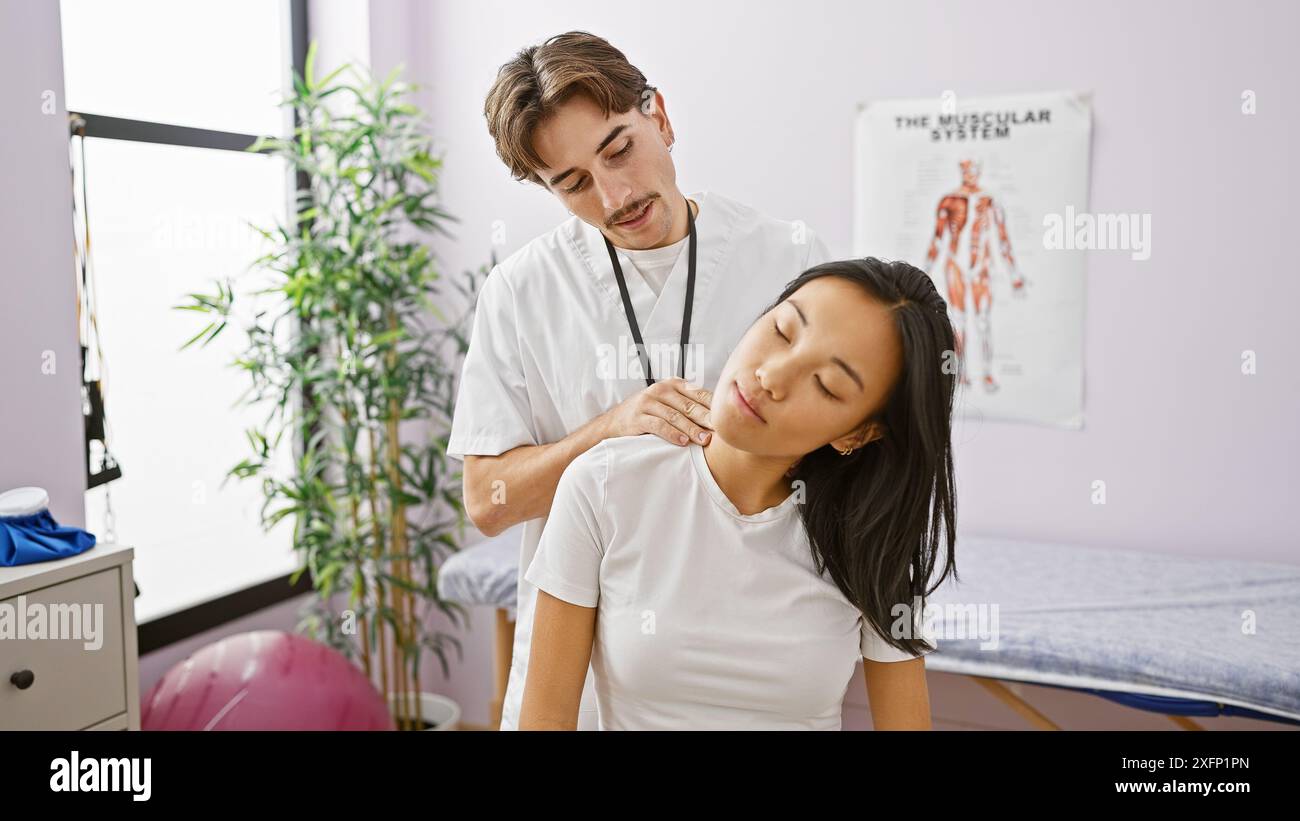 Un fisioterapista maschile esegue la terapia del collo su una paziente femminile in una clinica con un grafico del sistema muscolare visibile. Foto Stock