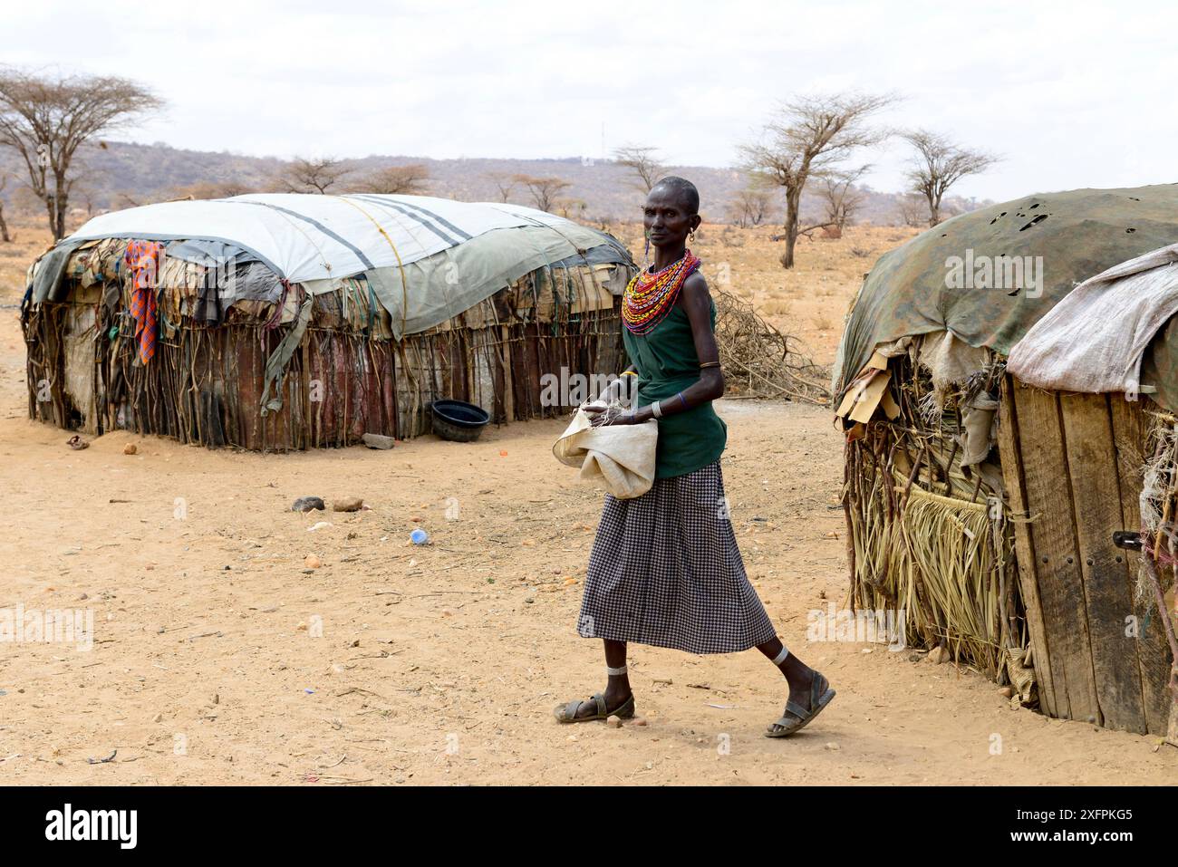Samburu Woman accanto a capanne improvvisate, in un paesaggio asciutto vicino alla riserva nazionale di Samburu, Kenya, settembre 2017. Foto Stock