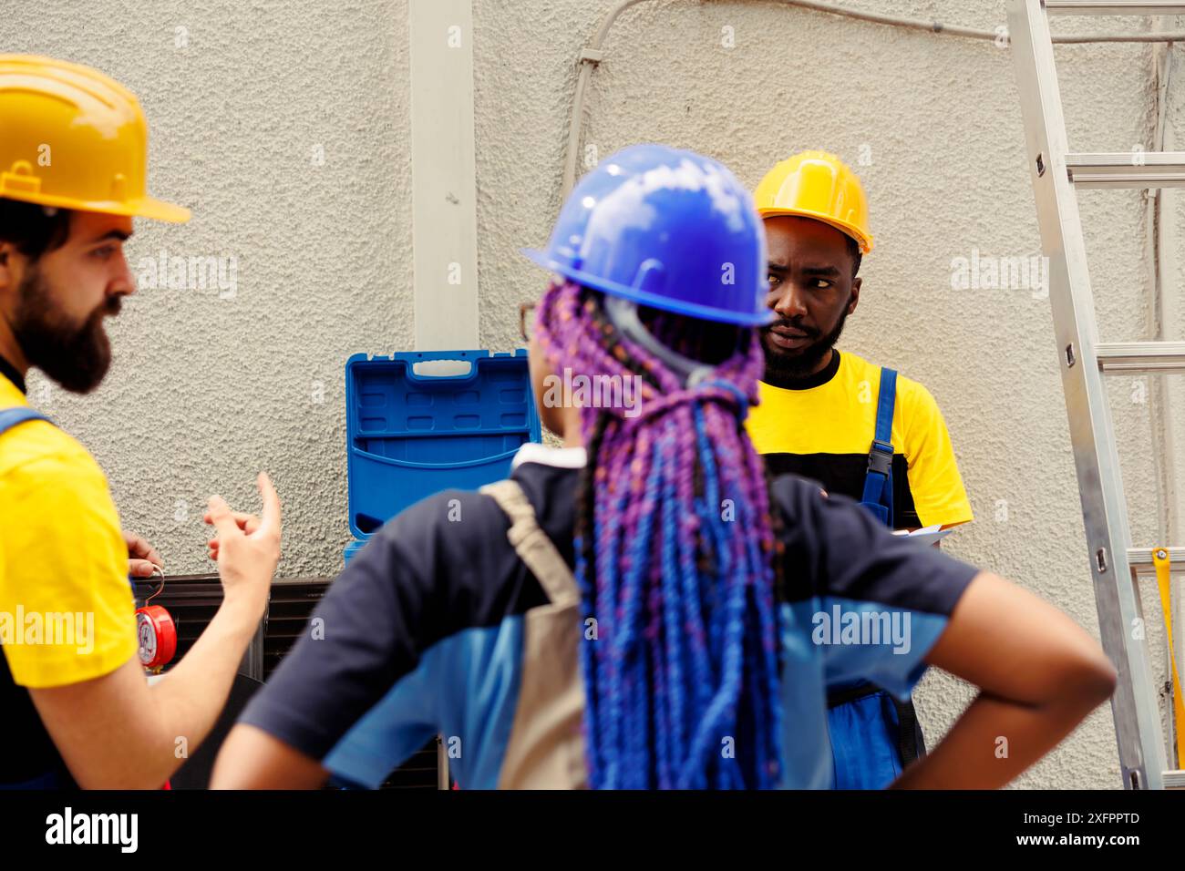 Team eterogeneo di elettricisti autorizzati a trovare soluzioni per riparare il condizionatore d'aria esterno fuori servizio. Tecnici qualificati incaricati dal proprietario di casa di riparare il sistema hvac danneggiato Foto Stock