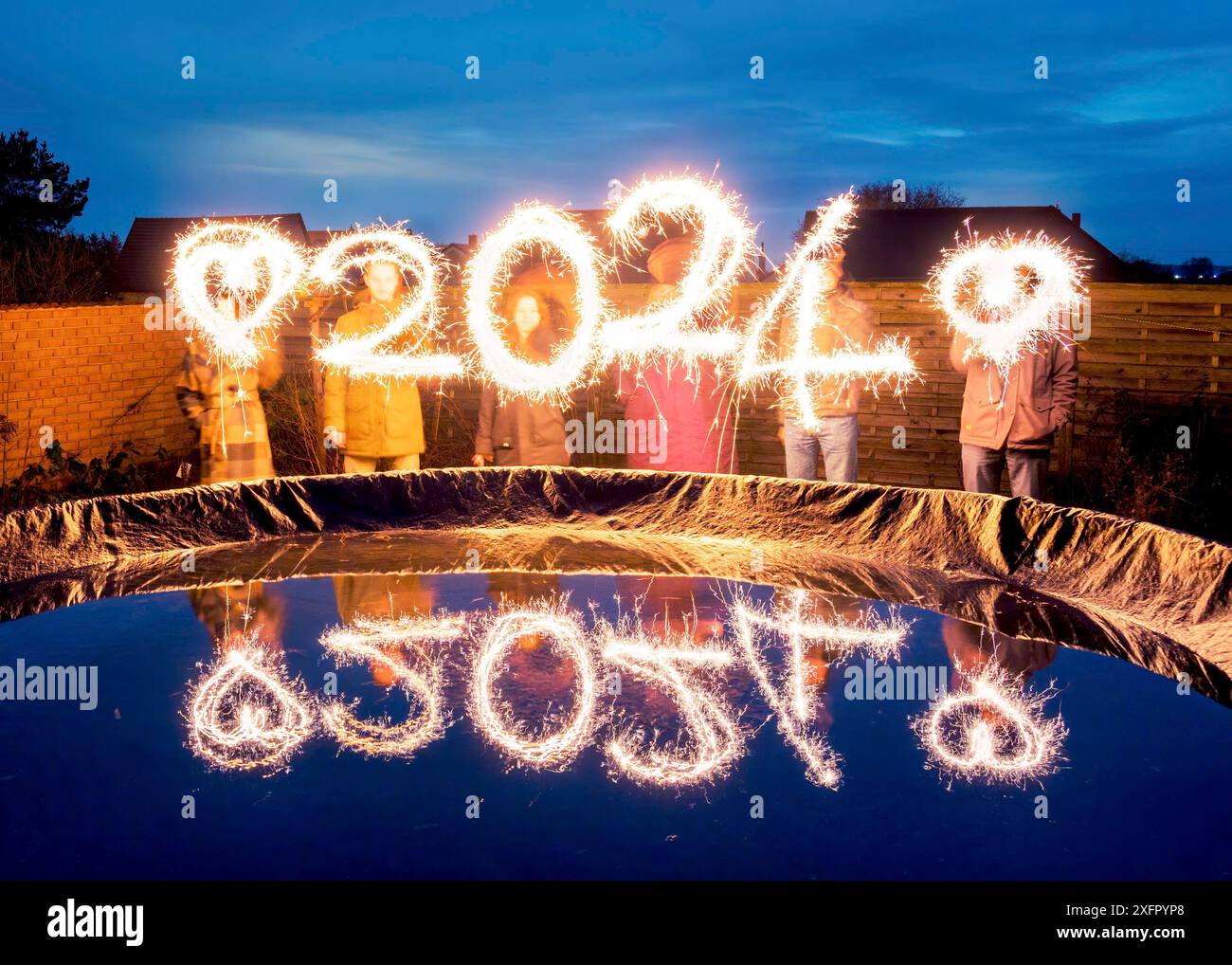 Persone con sparkler in mano che disegnano 2024 con scintille. Anno nuovo 2024, idea creativa Foto Stock