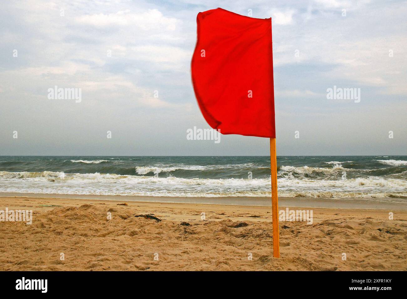 Una bandiera rossa è piantata nella sabbia, vietando il nuoto a causa delle acque scoscese Foto Stock