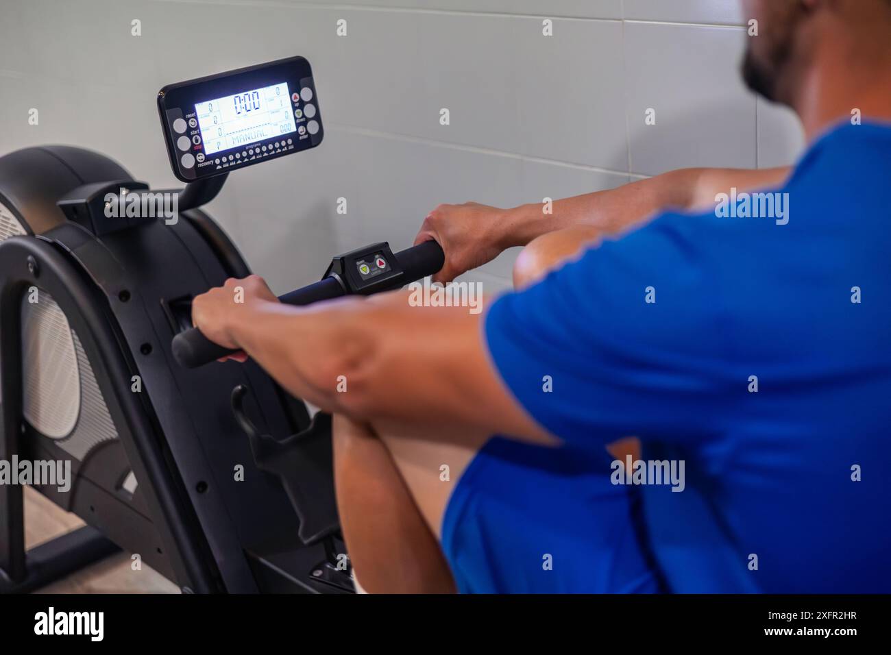 vista ravvicinata di un giovane atleta anonimo che esegue un esercizio aerobico su una vogatrice in palestra. Questa immagine acquisisce l'intensità e la messa a fuoco di Foto Stock