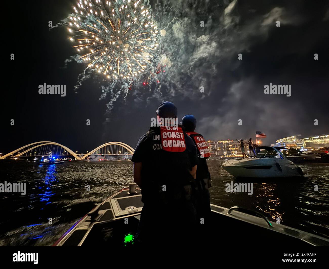 Da sinistra, il sottufficiale della Guardia Costiera degli Stati Uniti Justis Rodarte e il fornitore Seaman Zurwan, membri della stazione della Guardia Costiera degli Stati Uniti Washington D.C., osservano i fuochi d'artificio lungo il fiume Anacostia durante i fuochi d'artificio post-partita al Nationals Park, 3 luglio 2024. I membri hanno contribuito a far rispettare una zona di sicurezza fuori dal campo di baseball durante la celebrazione dei fuochi d'artificio. (Foto della Guardia Costiera degli Stati Uniti di Christopher Bokum, sottufficiale di terza classe) Foto Stock