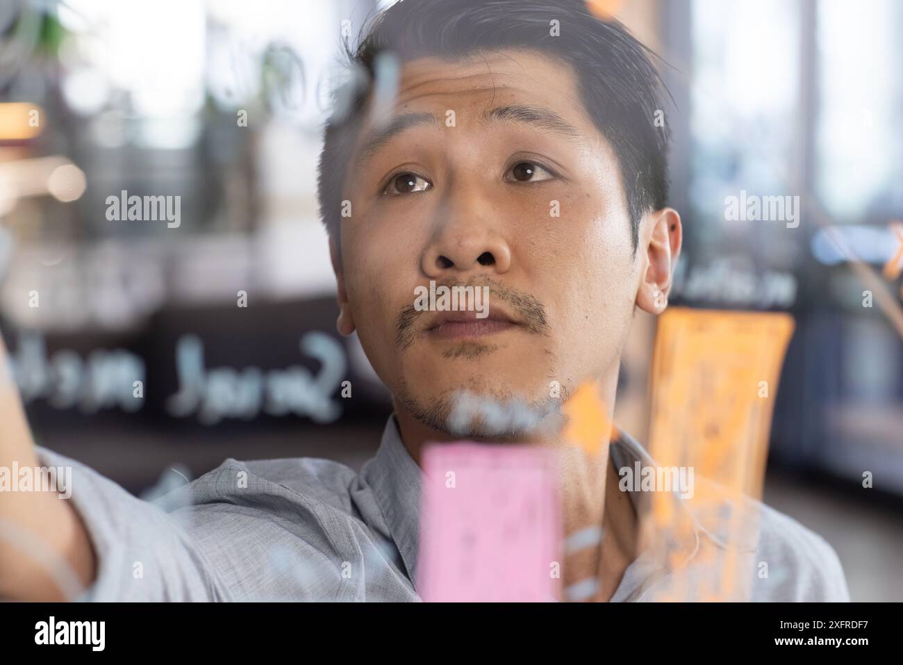 Scrivendo su una lavagna di vetro, un uomo che fa il brainstorming di idee in un moderno ambiente d'ufficio Foto Stock