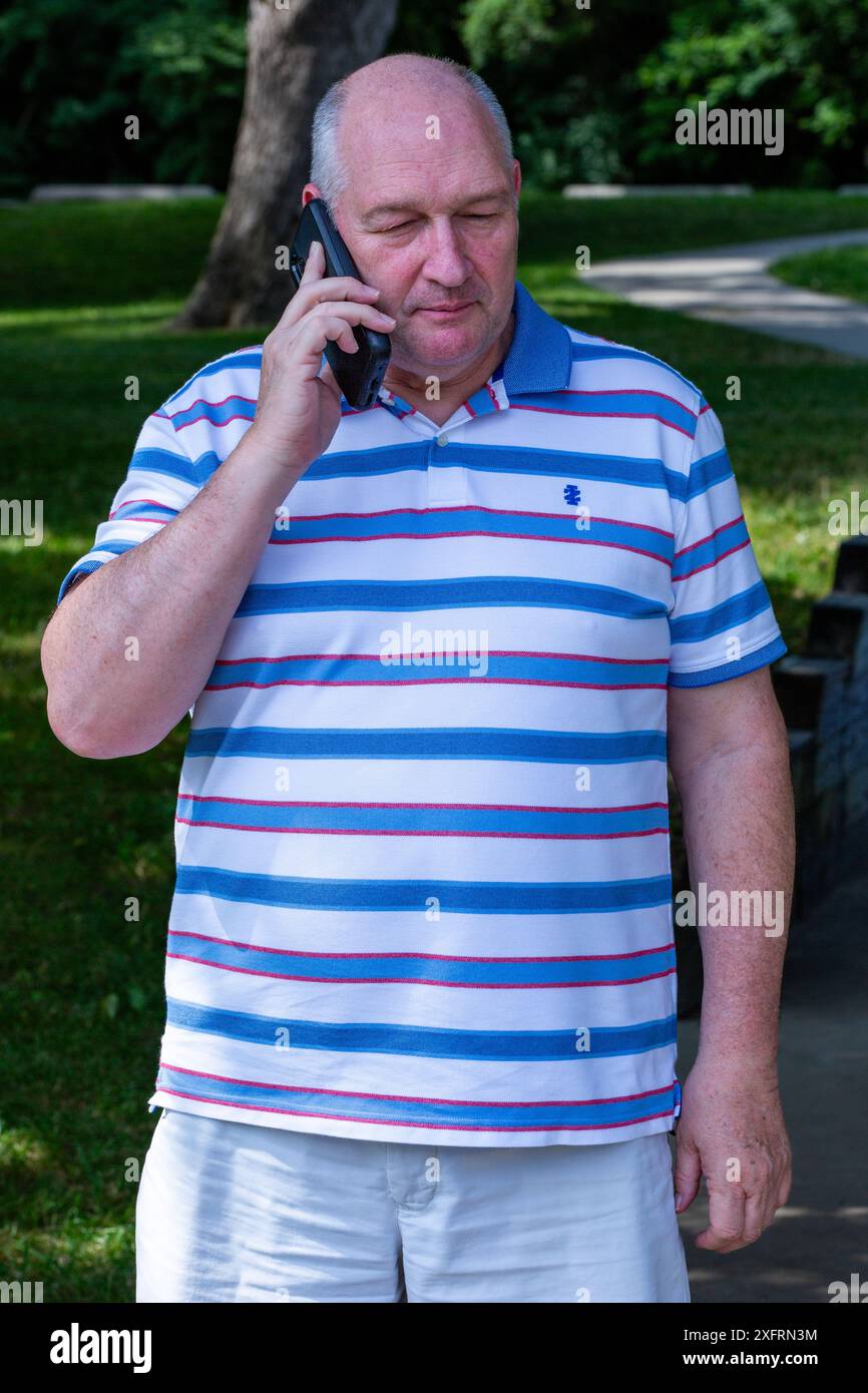 Un uomo calvo di mezza età con una camicia a righe che usa un cellulare. Foto Stock