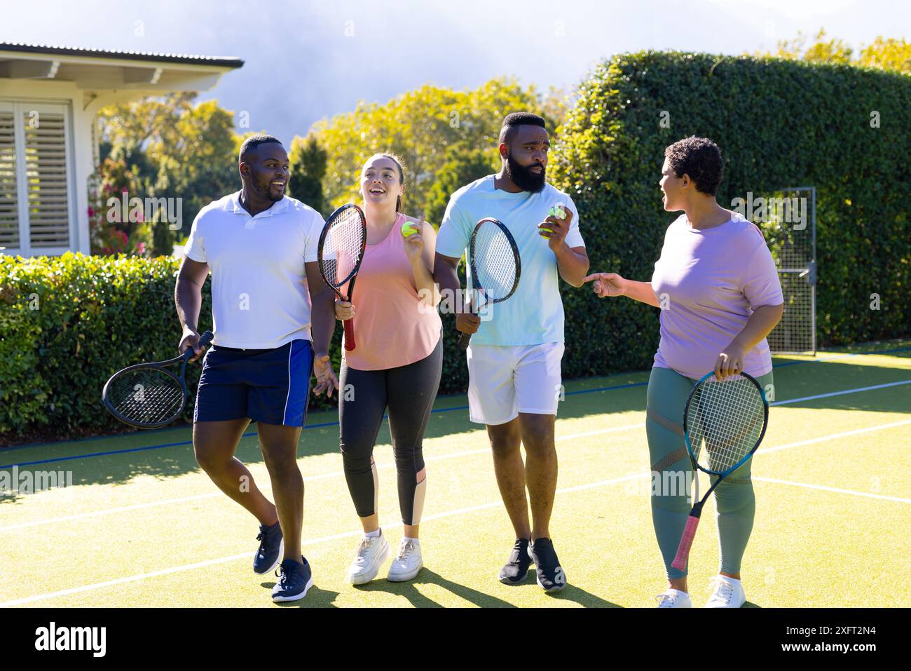 Giocando a tennis, un gruppo di amici diversi che tengono racchette e palle da tennis e si divertono all'aria aperta Foto Stock