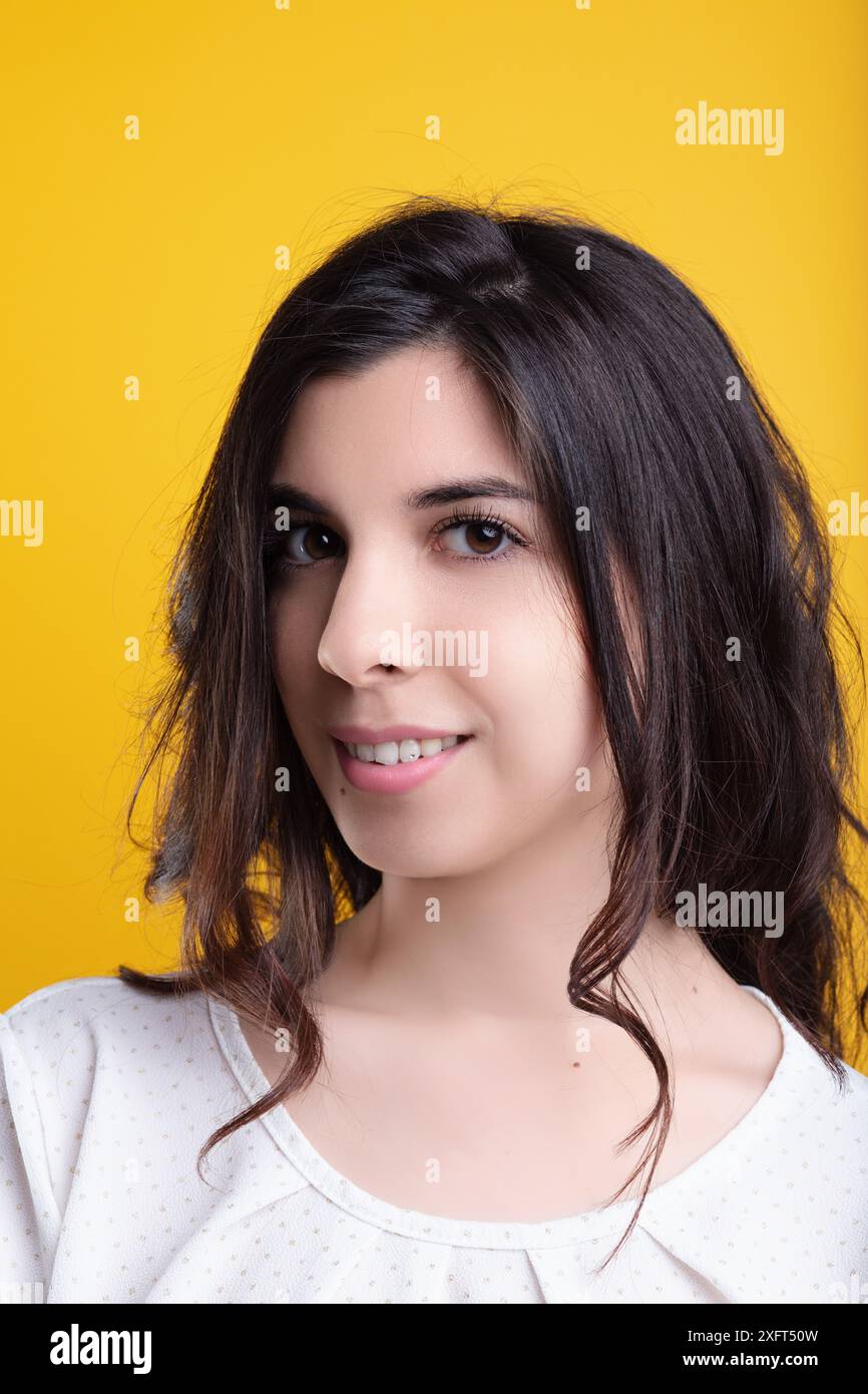 Giovane donna con lunghi capelli castani posa felicemente su sfondo giallo, irradiando gioia e positività Foto Stock