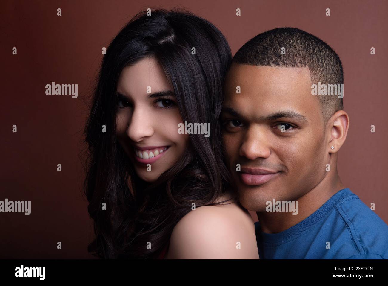 Coppia felice e interrazziale sorridente e abbracciata di fronte a un caldo sfondo marrone, che irradia amore e gioia in una romantica ripresa in studio Foto Stock