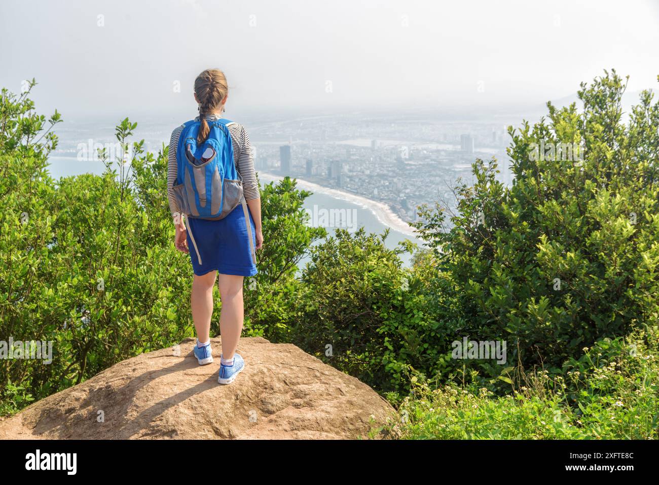 Giovane turista che gode di una splendida vista e di aria fresca sulla cima della montagna tra cespugli verdi. Ragazza con zaino blu. Foto Stock