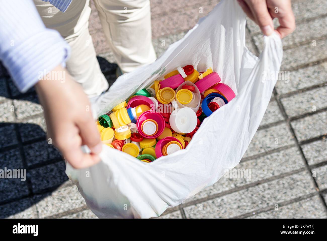 Mani femminili che tengono in mano un sacchetto di plastica riempito con tappi per bottiglie di plastica per il riciclaggio Foto Stock