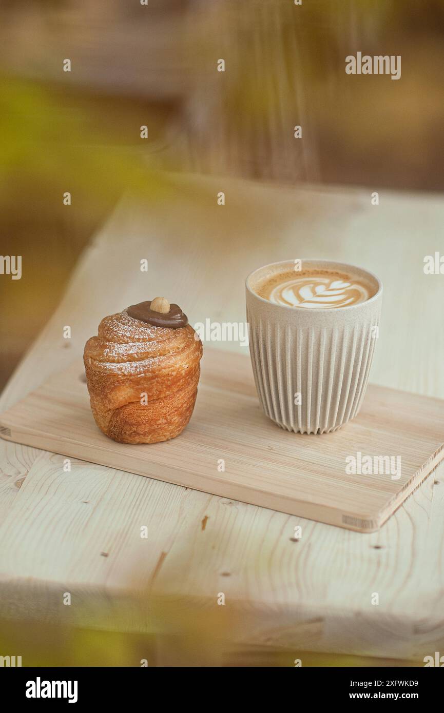 Cappuccino e cruffin su un tavolino minimalista. Stile di vita del bar. Messa a fuoco selettiva. Foto Stock