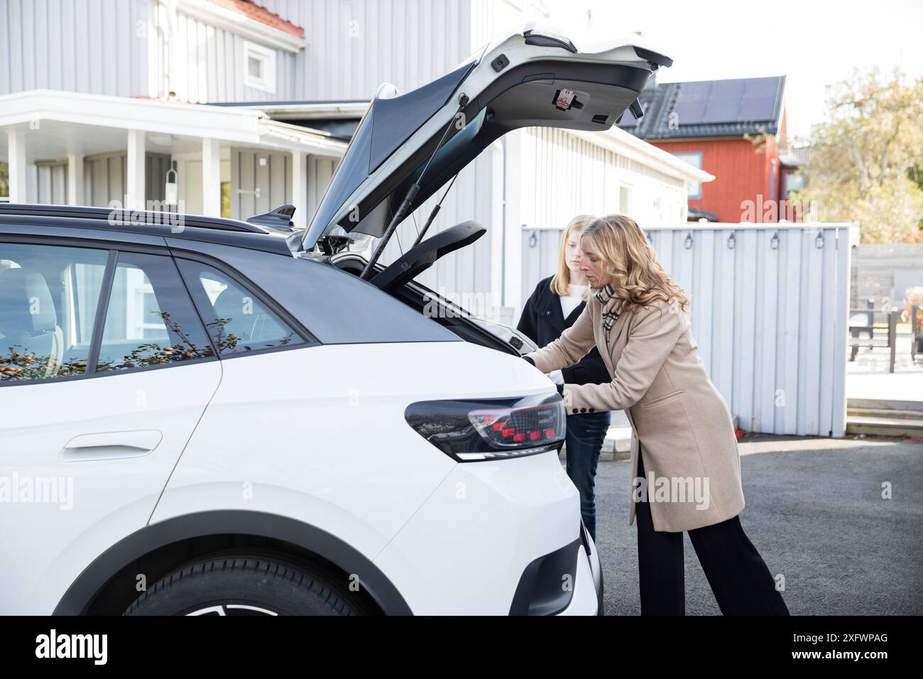 Madre e figlia caricano bagagli in auto elettrica Foto Stock