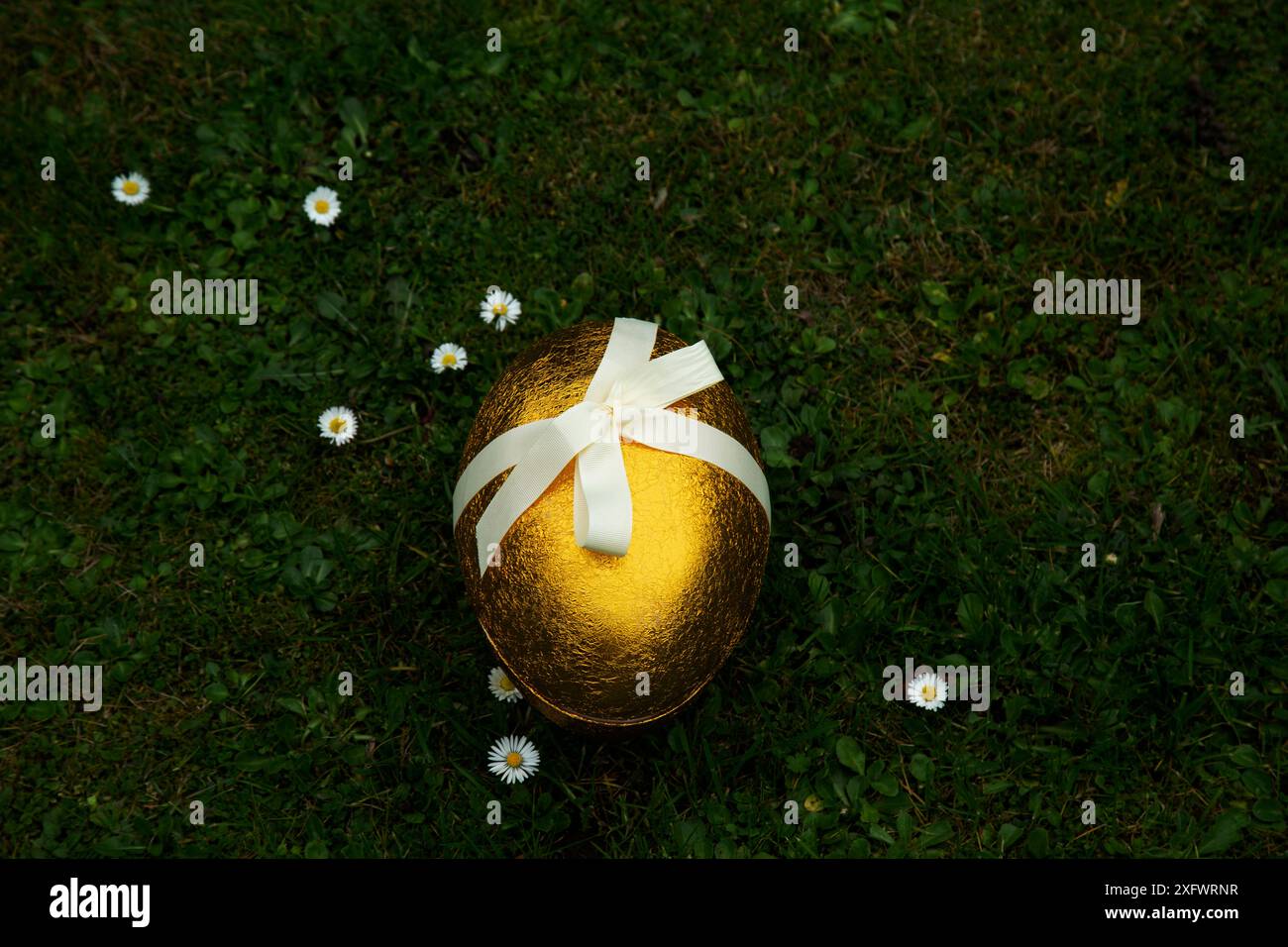 Uovo di Pasqua dorato con nastro legato sull'erba Foto Stock