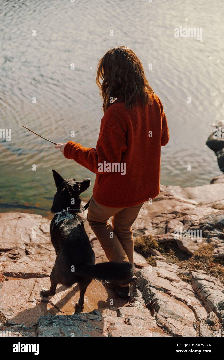 Vista posteriore di una giovane donna con un cane in piedi sulla riva del lago Foto Stock