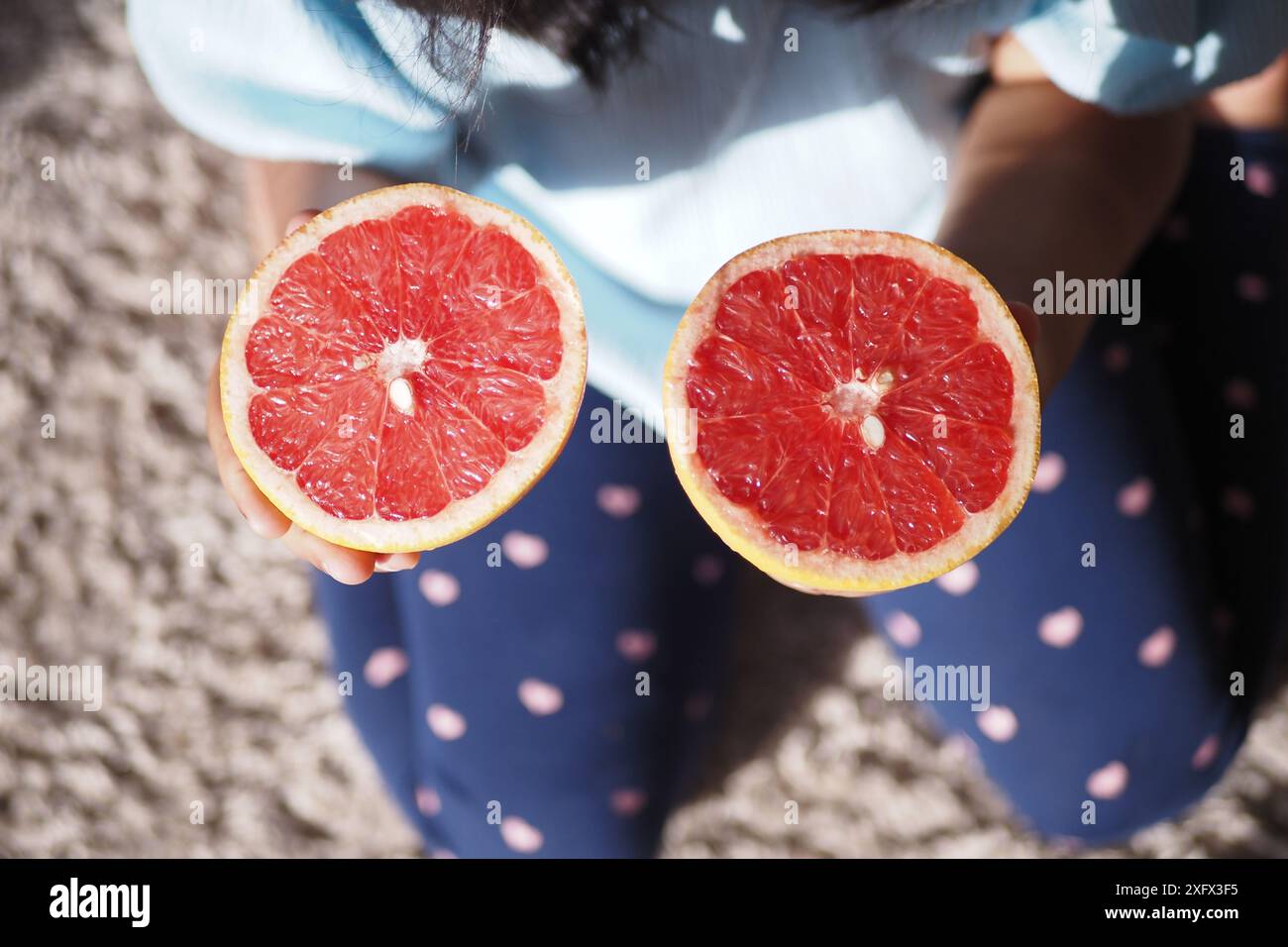 Una persona detiene due metà di un pompelmo rosso, un agrumato sano ricco di vitamine Foto Stock