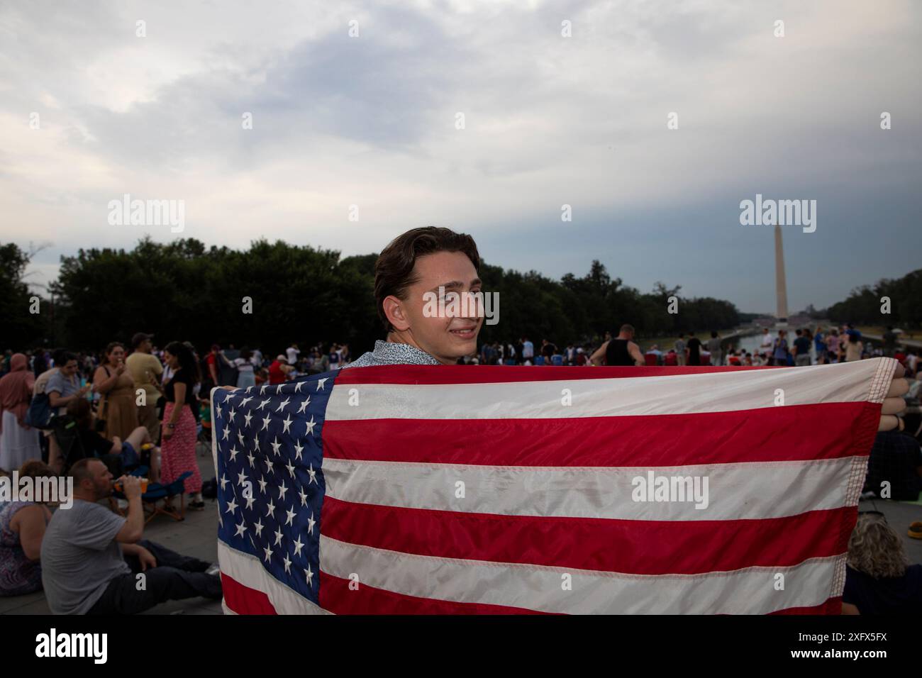 Washington DC, Stati Uniti. 4 luglio 2024. Una persona detiene la bandiera degli Stati Uniti mentre attende i fuochi d'artificio per celebrare il giorno dell'indipendenza degli Stati Uniti il 4 luglio 2024 a Washington DC. La capitale della nazione è stata decorata in rosso, bianco e blu giovedì mentre migliaia di persone si sono imbattute nel paese per festeggiare il 4 luglio. Crediti: SIPA USA/Alamy Live News Foto Stock