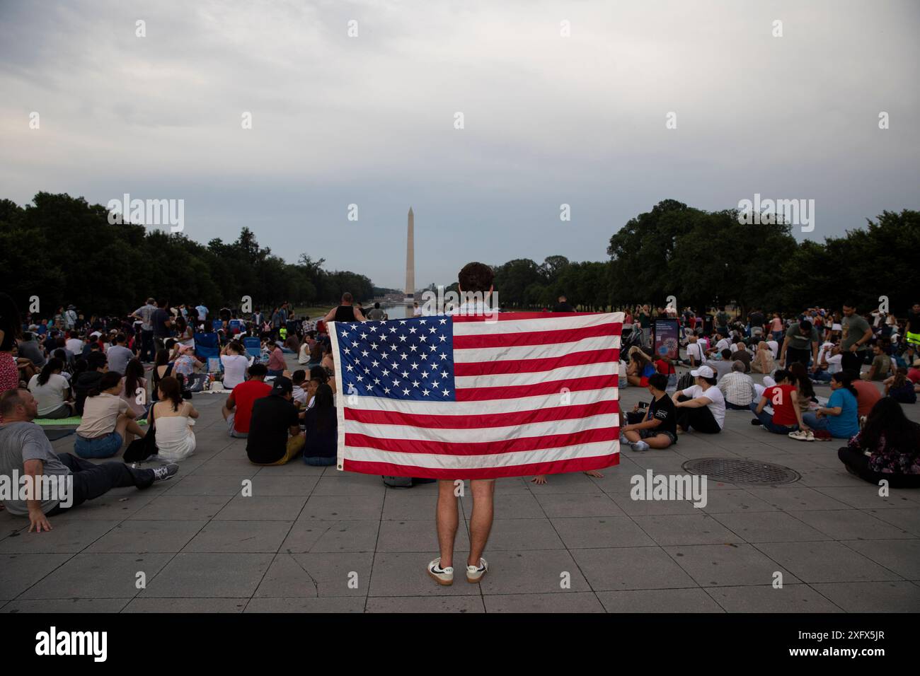 Washington DC, Stati Uniti. 4 luglio 2024. Una persona detiene la bandiera degli Stati Uniti mentre attende i fuochi d'artificio per celebrare il giorno dell'indipendenza degli Stati Uniti il 4 luglio 2024 a Washington DC. La capitale della nazione è stata decorata in rosso, bianco e blu giovedì mentre migliaia di persone si sono imbattute nel paese per festeggiare il 4 luglio. Crediti: SIPA USA/Alamy Live News Foto Stock