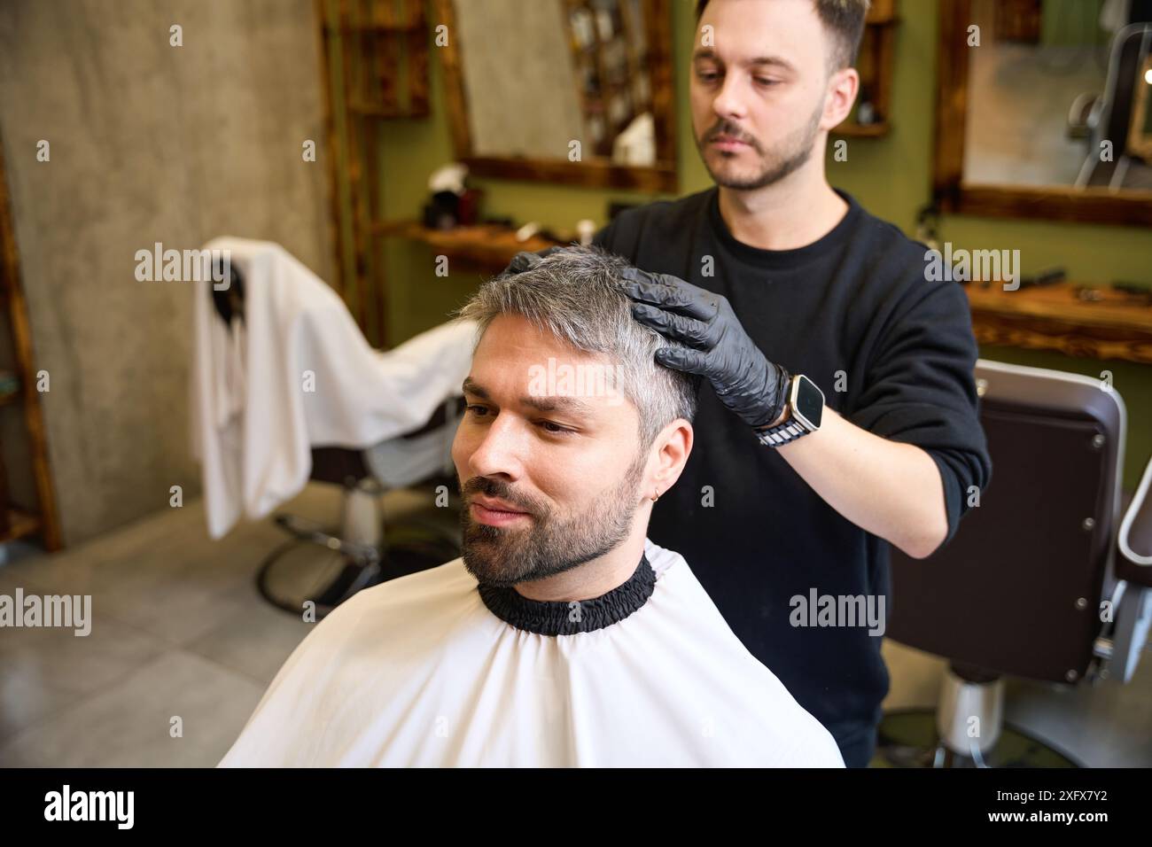 Barbiere esperto che massaggiava la testa di un cliente adulto dopo il taglio di capelli Foto Stock