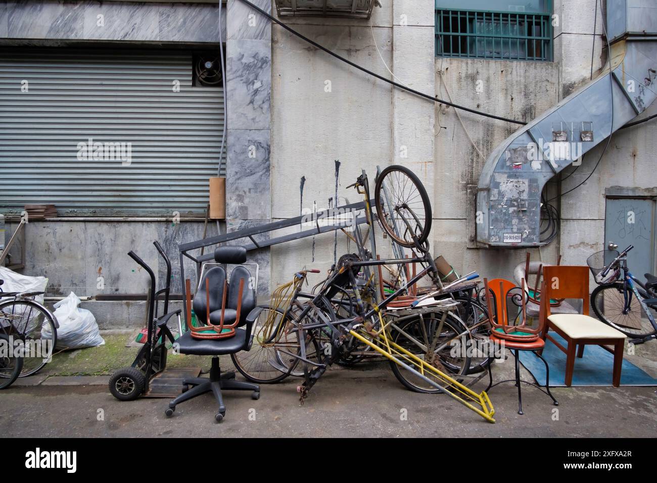 Scena di degrado urbano con biciclette scartate e mobili contro la facciata dell'edificio intemprata Foto Stock