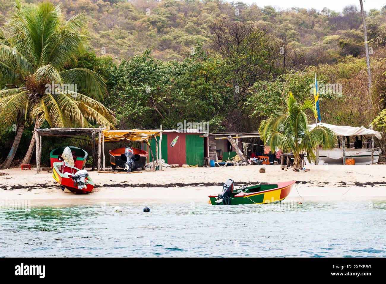 Colorata scena di spiaggia a Salt Whistle Bay, Mayreau, con molo, sarong, bar e negozio souvenir. Saint Vincent e Grenadine. Foto Stock