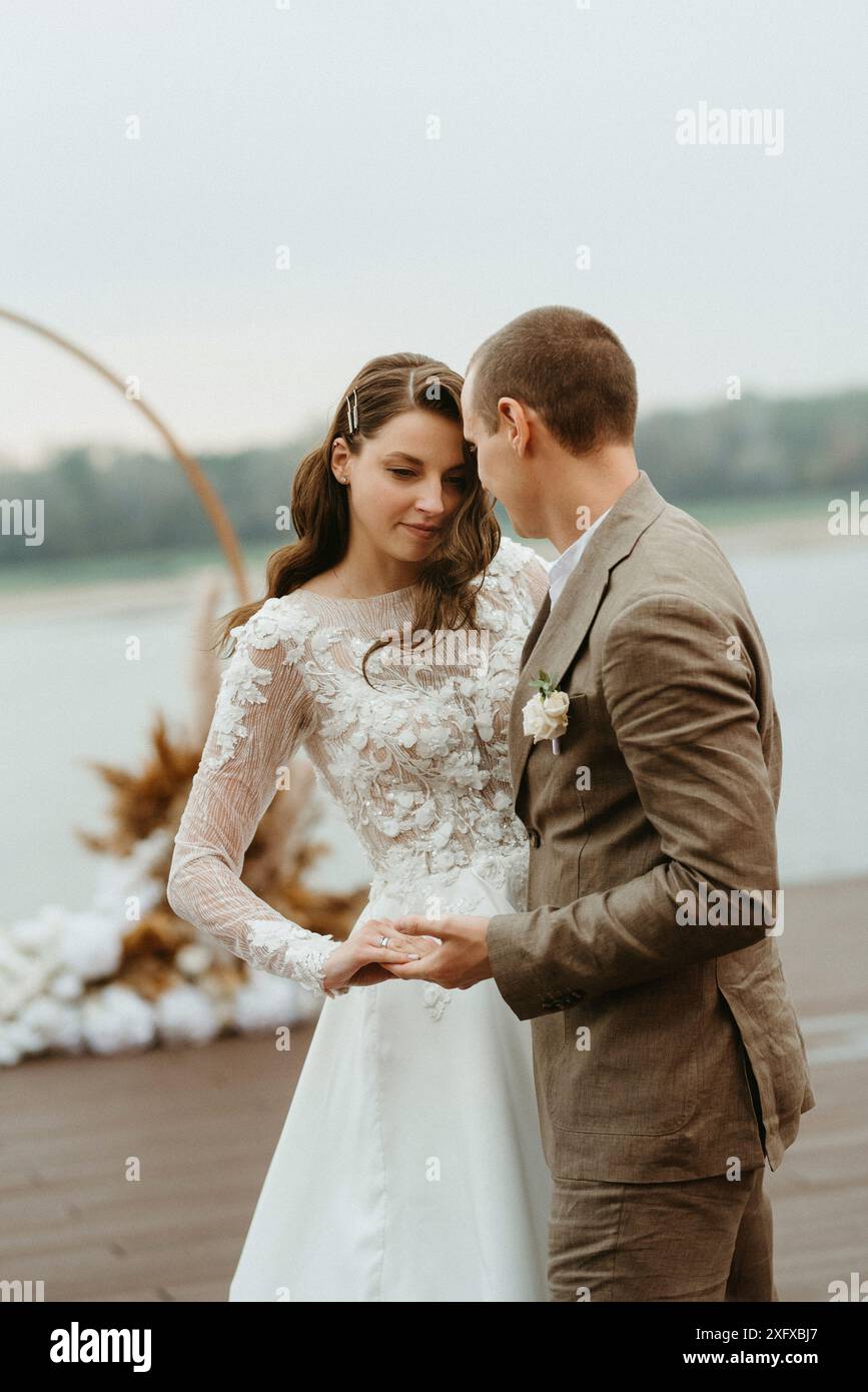 il primo ballo nuziale della sposa e dello sposo sul molo vicino al fiume, sullo sfondo dell'arco nuziale Foto Stock