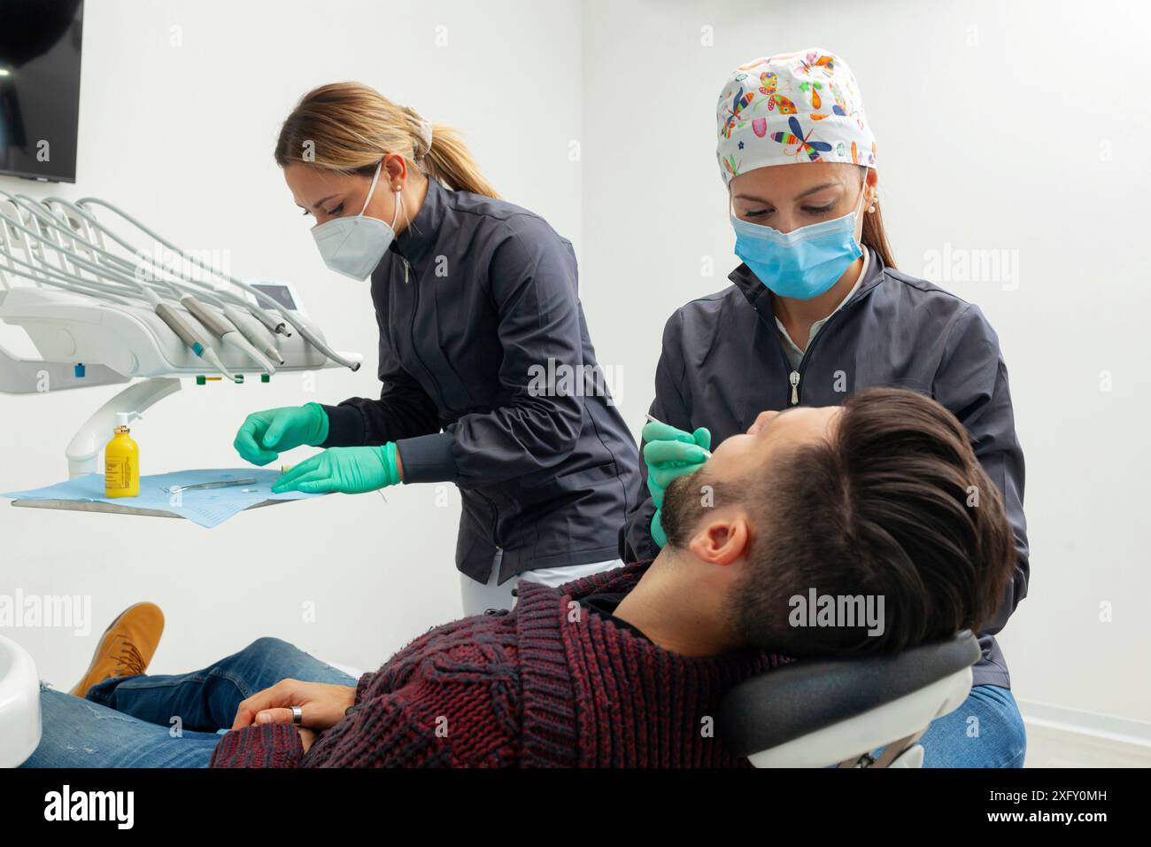 Il dentista femminile esamina un paziente in un ufficio dentistico utilizzando strumenti professionali e dispositivi di protezione personale. Foto Stock