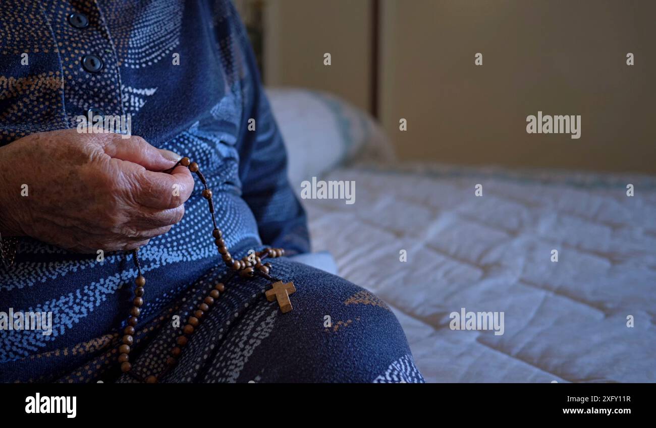 Donna anziana di 70-80 anni prega con il rosario a casa. Foto Stock