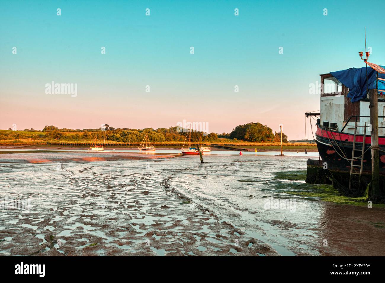 Tramonto sulle distese fangose durante la bassa marea vicino a una casa galleggiante ormeggiata a Woodbridge, Tide Mill Harbour, River Debden, Woodbridge, Suffolk, Inghilterra Regno Unito Foto Stock