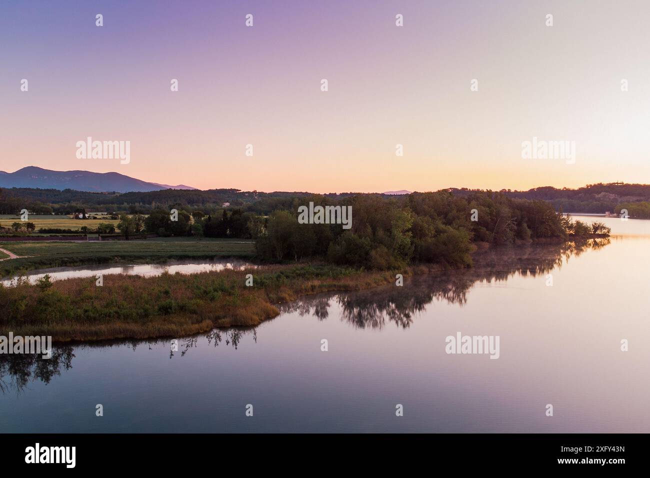 Vista aerea del lago Banyoles all'alba a Girona, Catalogna, Spagna. Ripresa in droni di un tranquillo paesaggio lacustre al mattino con luce calda al tramonto Foto Stock