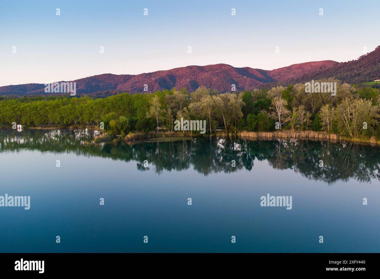 Vista aerea del lago Banyoles all'alba a Girona, Catalogna, Spagna. Ripresa in droni di un tranquillo paesaggio lacustre al mattino con luce calda al tramonto Foto Stock