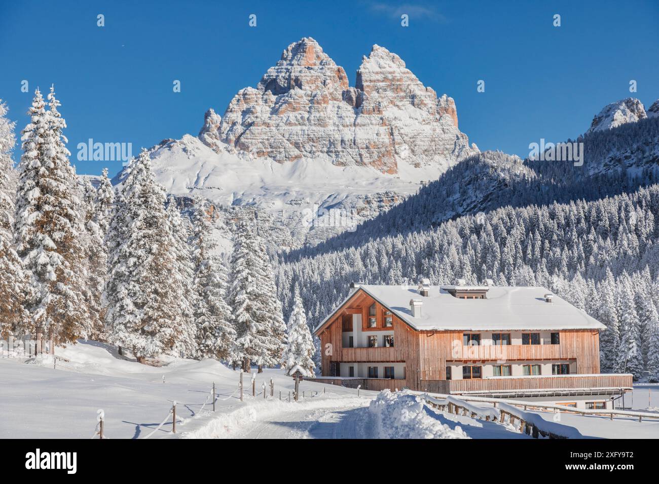 Italia, Veneto, provincia di Belluno, Auronzo di Cadore, Dolomiti - strada innevata e struttura ricettiva per turisti a Misurina, panorama invernale con sullo sfondo le iconiche tre Cime di Lavaredo Foto Stock