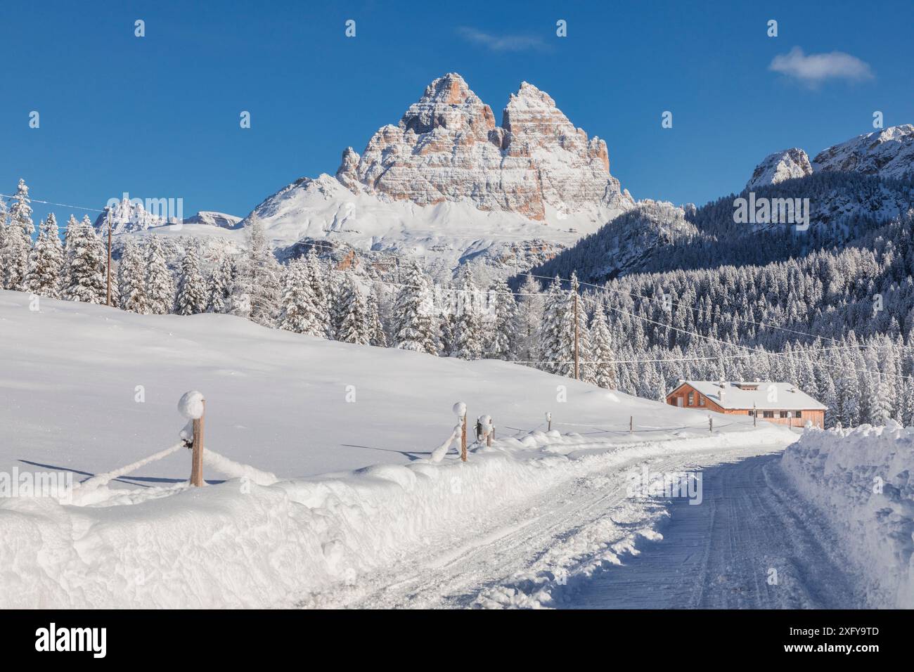 Italia, Veneto, provincia di Belluno, Auronzo di Cadore, Dolomiti - strada innevata e struttura ricettiva per turisti a Misurina, panorama invernale con sullo sfondo le iconiche tre Cime di Lavaredo Foto Stock