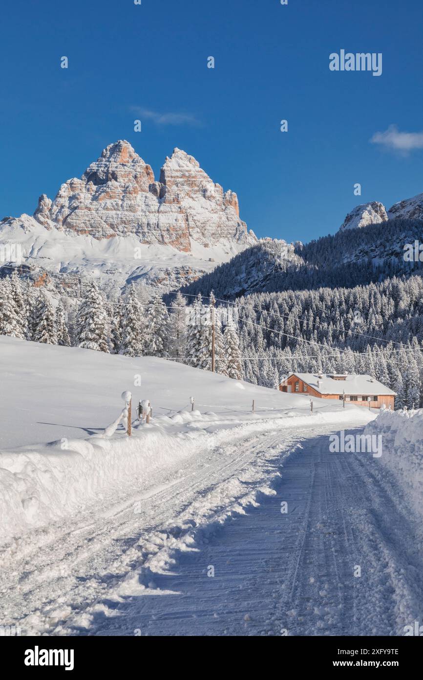 Italia, Veneto, provincia di Belluno, Auronzo di Cadore, Dolomiti - strada innevata e struttura ricettiva per turisti a Misurina, panorama invernale con sullo sfondo le iconiche tre Cime di Lavaredo Foto Stock