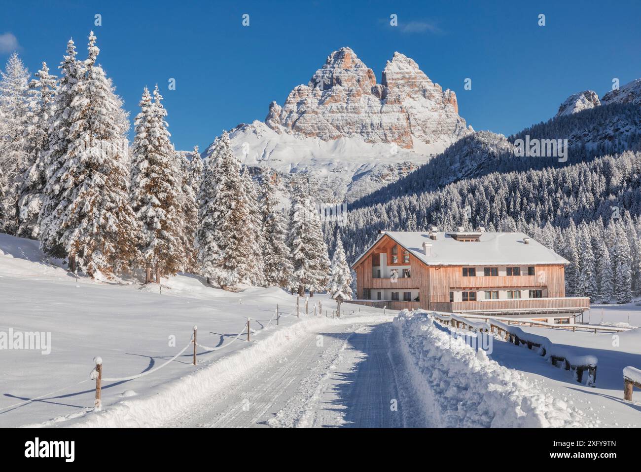 Italia, Veneto, provincia di Belluno, Auronzo di Cadore, Dolomiti - strada innevata e struttura ricettiva per turisti a Misurina, panorama invernale con sullo sfondo le iconiche tre Cime di Lavaredo Foto Stock