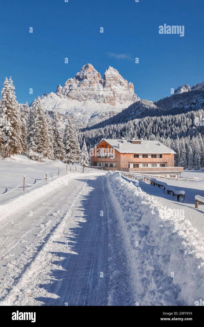 Italia, Veneto, provincia di Belluno, Auronzo di Cadore, Dolomiti - strada innevata e struttura ricettiva per turisti a Misurina, panorama invernale con sullo sfondo le iconiche tre Cime di Lavaredo Foto Stock
