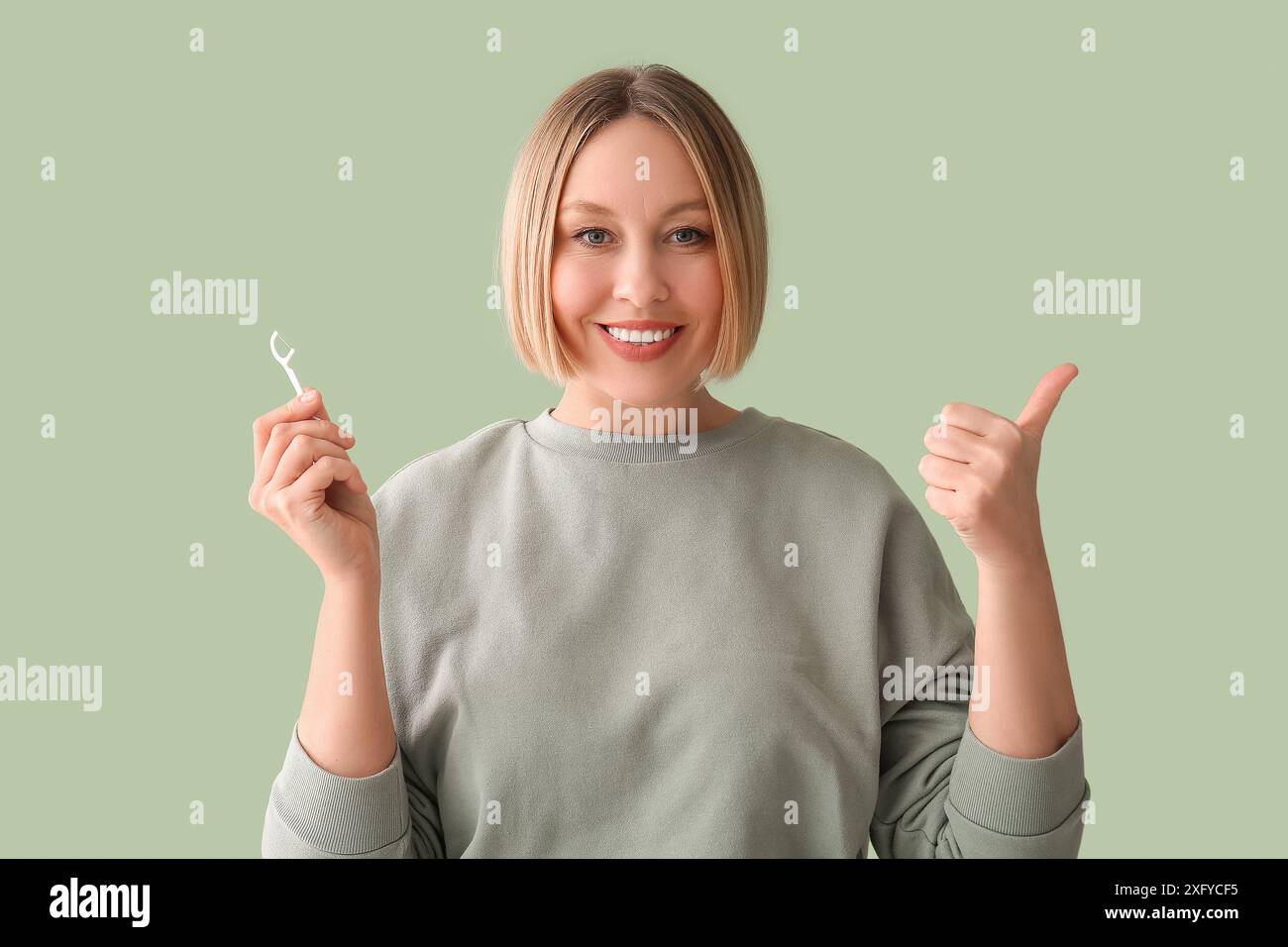 Donna con il filo interdentale che mostra il pollice su sfondo verde Foto Stock