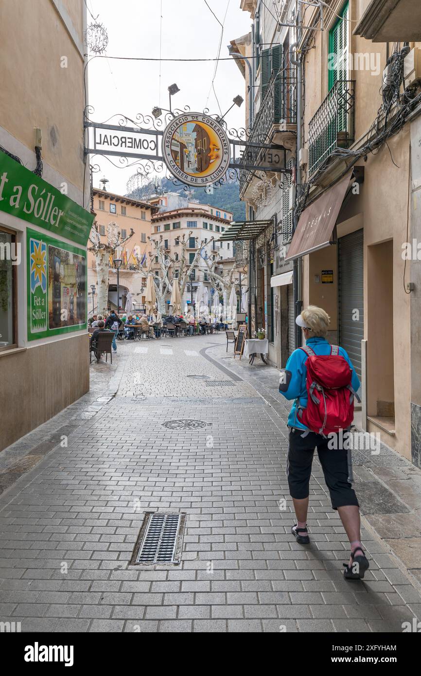 Donna con zaino che cammina dalla via dello shopping Carrer de sa Lluna (Moon Street) a Plaza de la Constitucion nel centro della città, Soller, regione di Serra de Tramuntana, Maiorca, Isole Baleari, Spagna, Europa Foto Stock