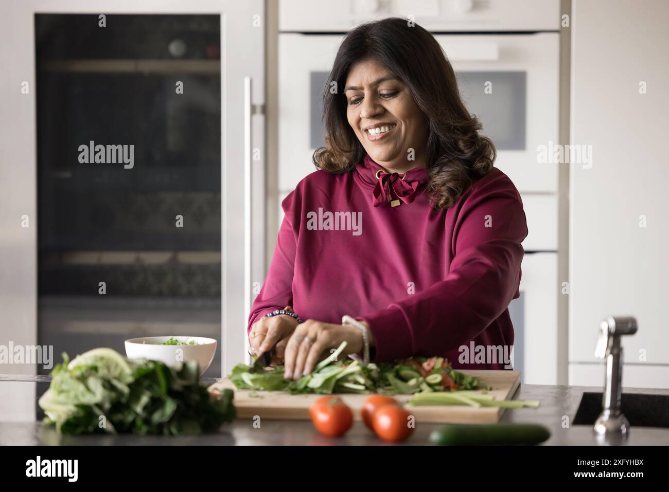 Chef indiano senior positivo che cucina insalata di verdure fresche Foto Stock