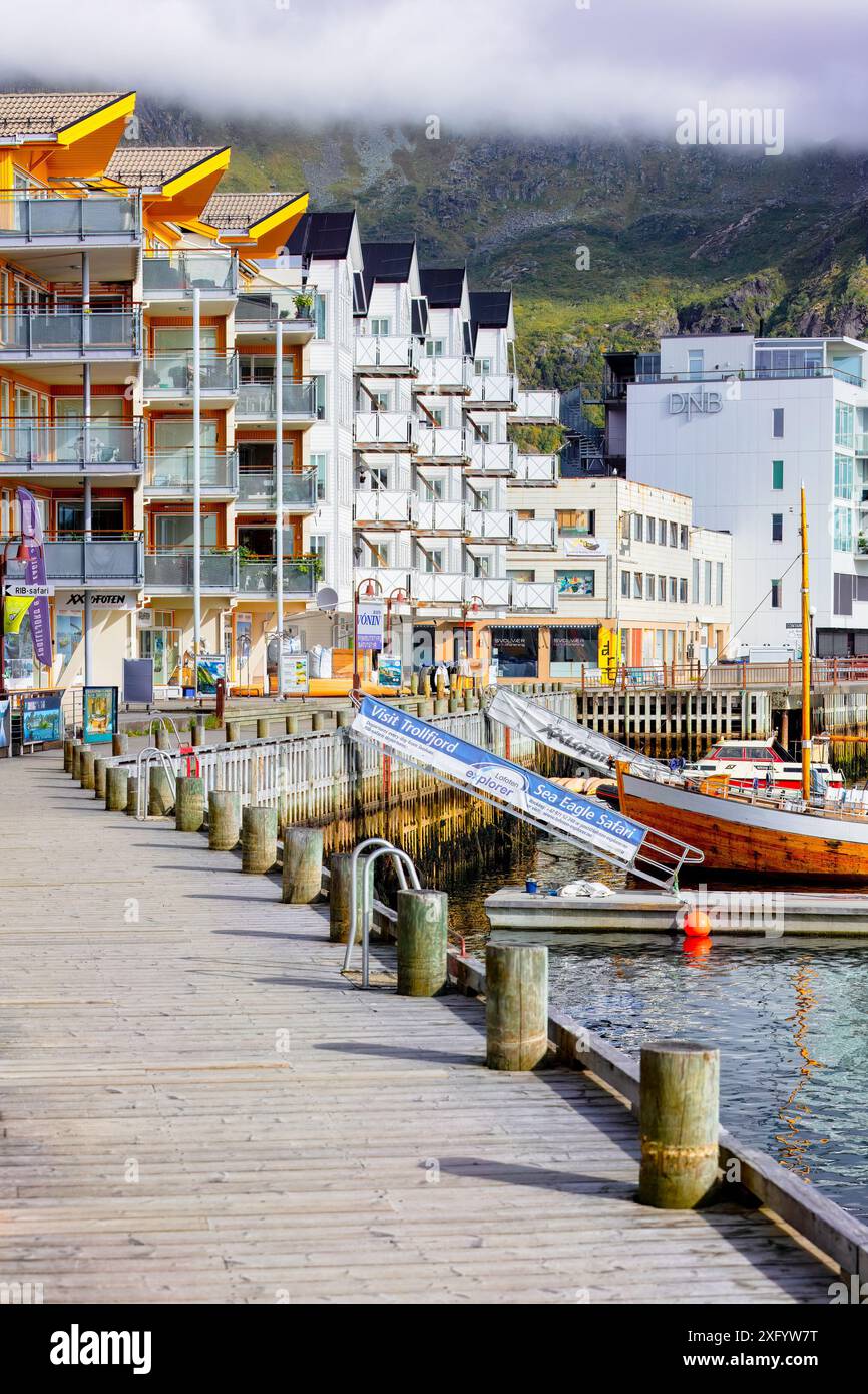 Sul lungomare della città di Svolvær, con edifici e barche moderni e colorati, montagne nebbiose sullo sfondo. Concetto di viaggio per destinazioni fredde alla moda. Foto Stock