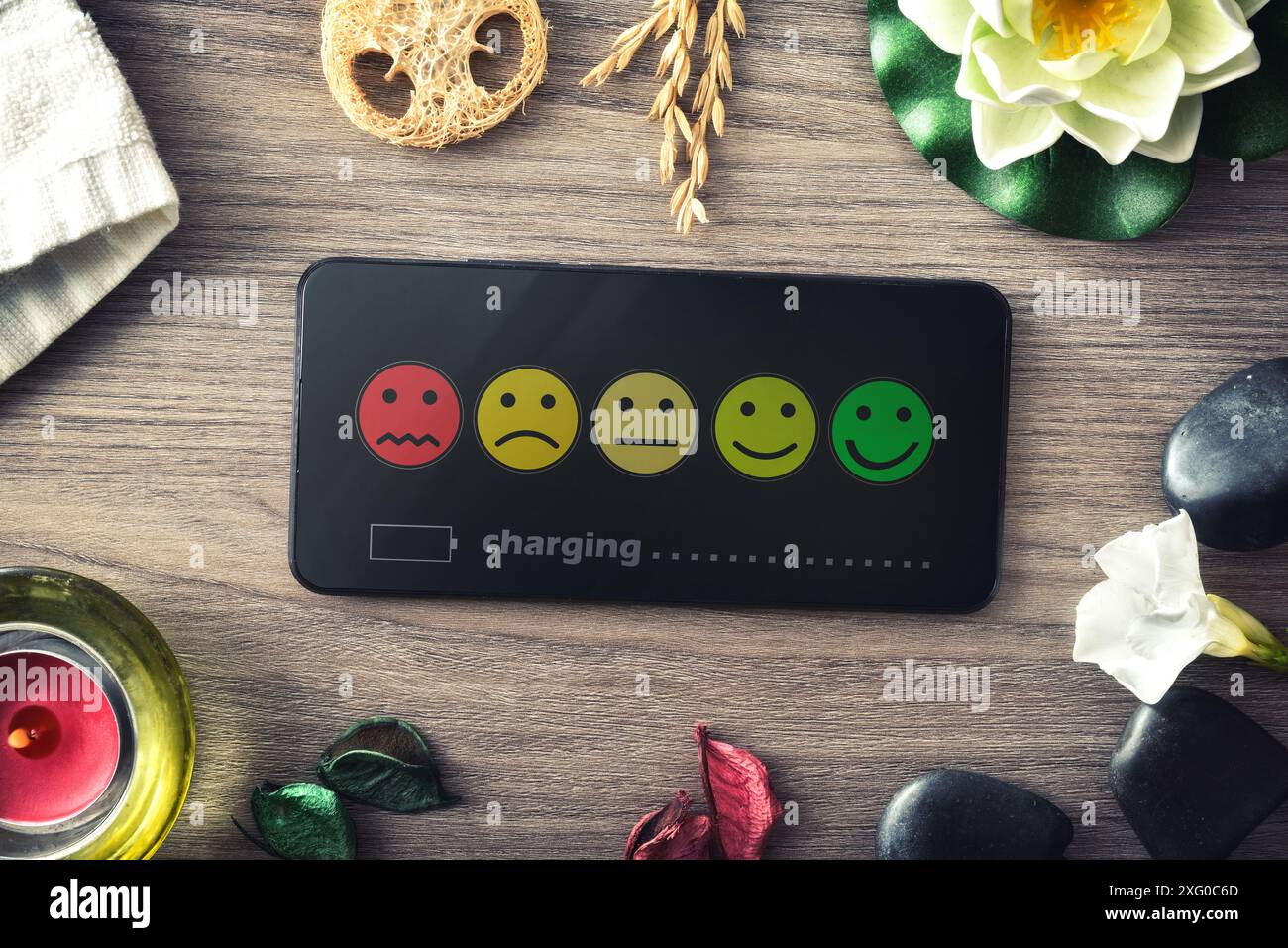 Concetto di benessere emotivo con emoticon su schermo mobile con simbolo di carico e elementi di benessere e relax su un tavolo di legno. Foto Stock