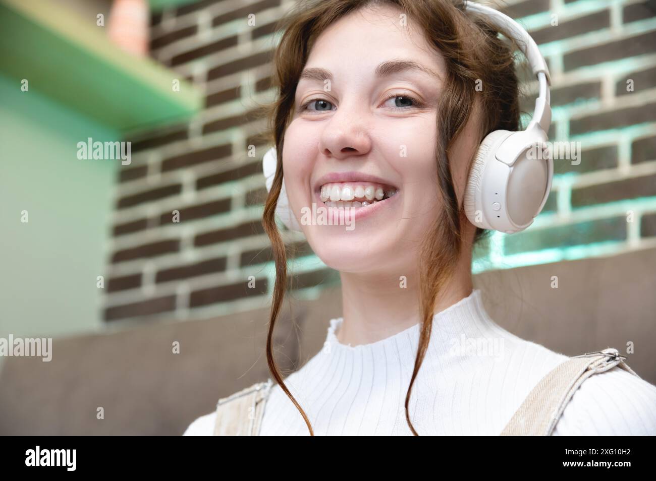 Ritratto di una giovane donna caucasica sorridente con le cuffie che parla tramite videochiamata da casa. Foto di una donna felice in cuffia che guarda la fotocamera Foto Stock