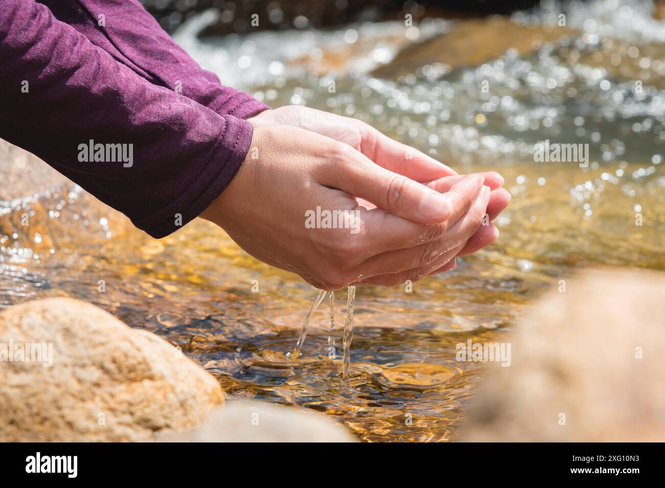 Primo piano di gocce d'acqua che cadono dalle mani femminili in un ruscello. La mano tocca l'acqua dolce. Un turista beve l'acqua da un serbatoio nel Foto Stock