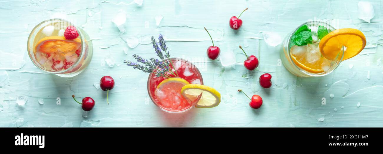 Cocktail estivi o mocktail panoramici, bevande fredde con agrumi, lavanda e ciliegie, scattate dalla cima su uno sfondo blu, un panorama Foto Stock