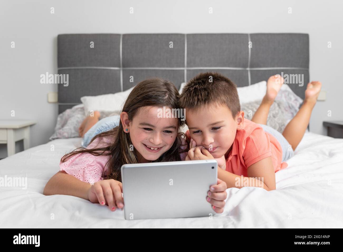 Bambini piccoli carini con un tablet digitale che utilizza Internet a casa. Sorellina caucasica e fratelli che navigano su Internet, guardano animati Foto Stock