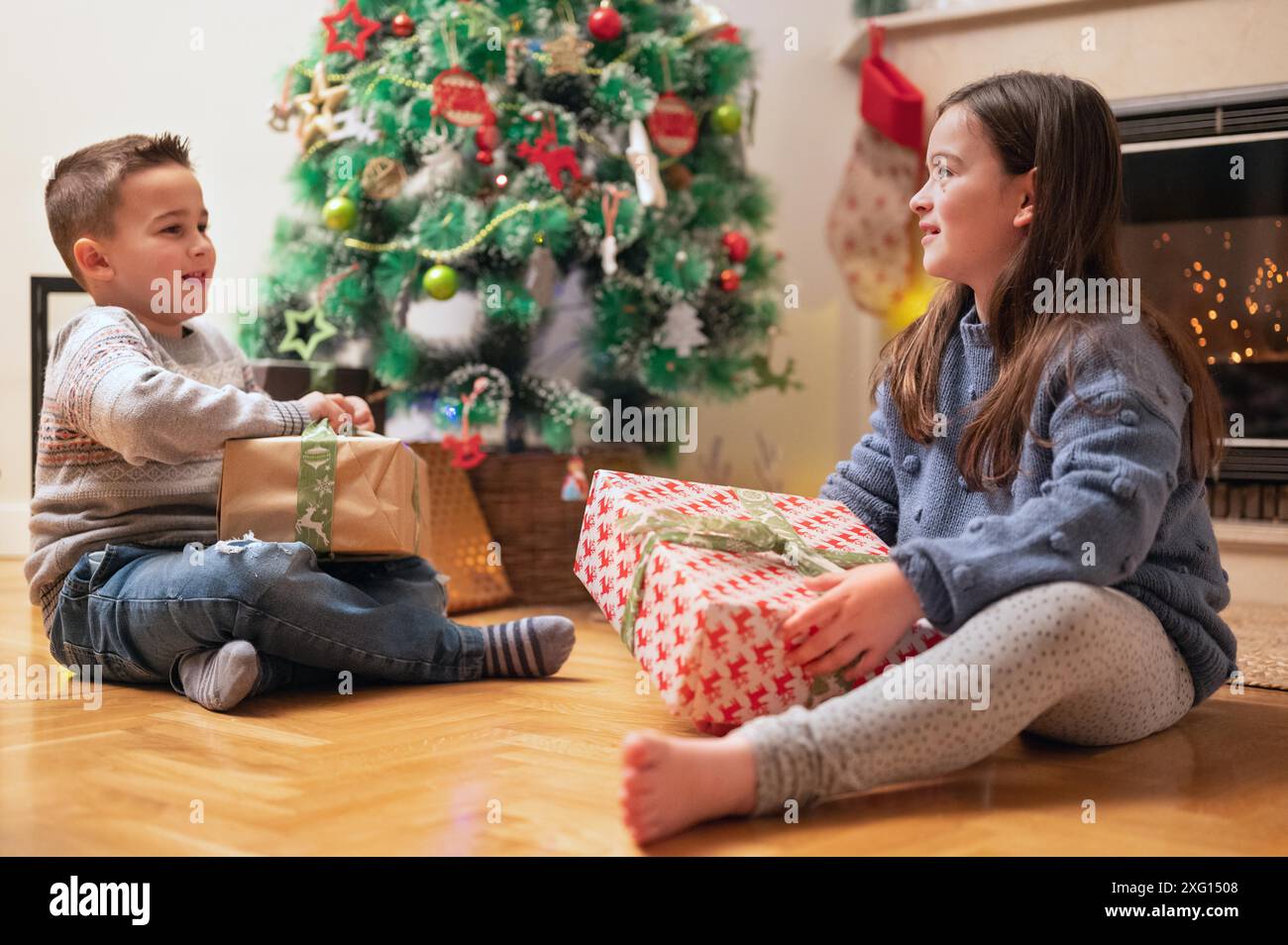 Bambini felici che aprono i regali di natale a casa vicino all'albero di Natale e al caminetto. Fotografia di alta qualità Foto Stock