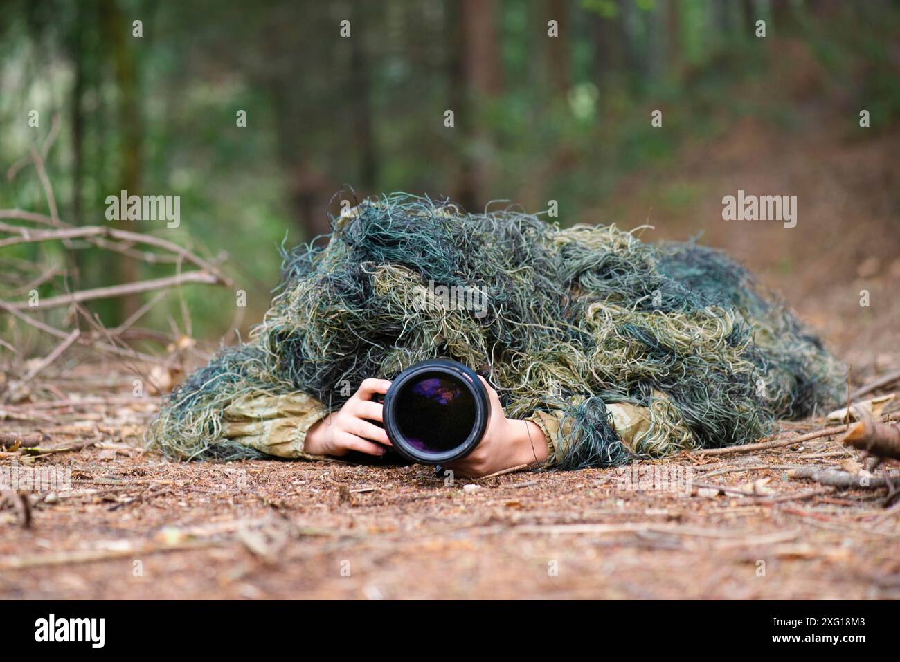 Fotografo che indossa abiti camouflage nella foresta, fotografia di animali selvatici con una macchina fotografica e teleobiettivo Foto Stock