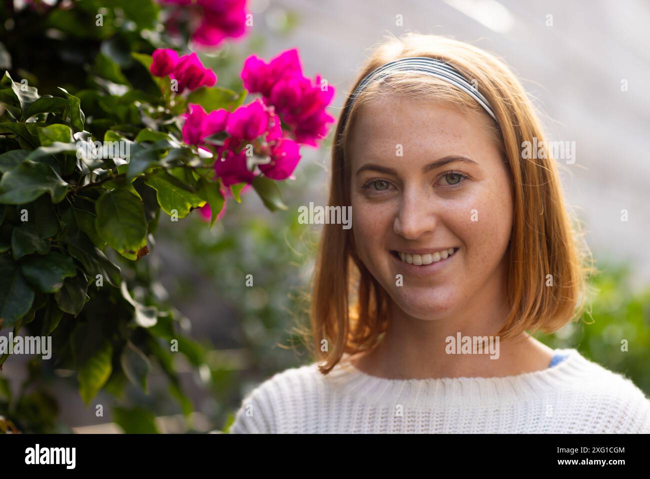 Donna sorridente con fascia in piedi accanto a vivaci fiori rosa all'aperto, spazio copia Foto Stock