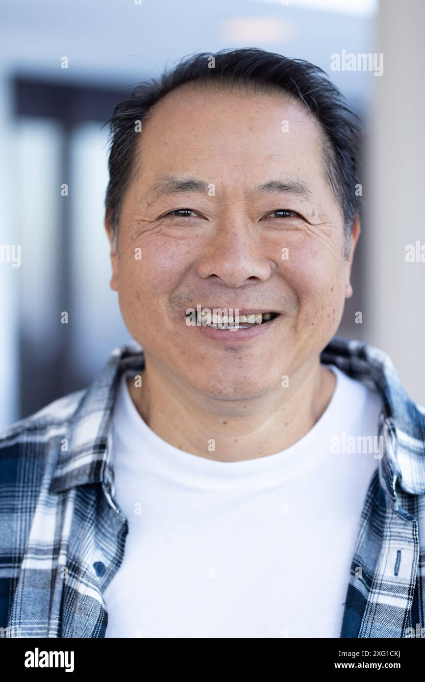 Un anziano sorridente che indossa una camicia a quadri e una t-shirt bianca, godendosi la vacanza Foto Stock
